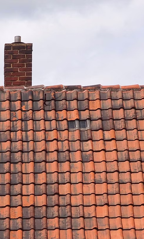 Close-up of ageing red clay roof tiles and a chimney stack showing signs of wear